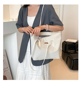 Detailed close-up of white woven tote bag featuring a metallic buckle and long straps
