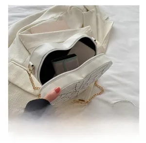 Detail showing internal capacity of white heart-shaped crossbody bag with gold chain