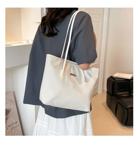 Dettaglio di una borsa tote bianca intrecciata con logo in metallo dorato e spalline lunghe