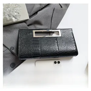 Detail of black crocodile-embossed clutch bag featuring a rectangular silver metal handle