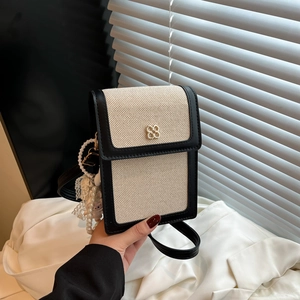 Chic beige canvas crossbody bag with black leather trim and a golden clover buckle detail