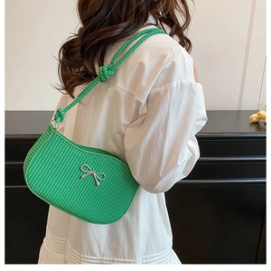 Close-up of green woven bag featuring silver bow detail and thick knotted shoulder strap