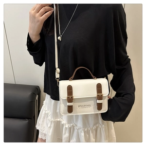 Detail of white square crossbody bag with brown leather straps and gold metal buckles