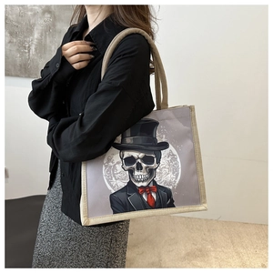 Detail of grey canvas tote bag with gothic skull graphic and beige woven handles
