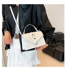 Detail of white crocodile embossed crossbody bag with golden lock and top handle