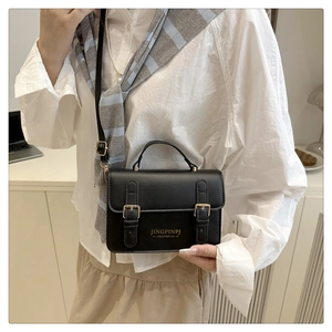 Detail of minimalist black leather crossbody bag with golden buckles and top handle
