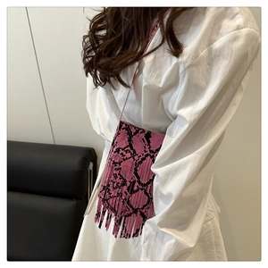 Detail of pink and black snakeskin pattern crossbody bag featuring long hanging tassels