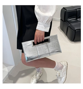Detail view of silver crocodile pattern clutch with metallic handle held by a model