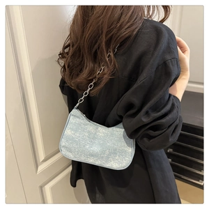 Close-up of light blue denim crescent bag with silver chunky chain strap on shoulder