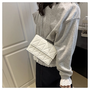 Detail showing the white geometric quilted texture and silver chain strap on the bag