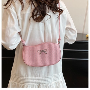 Pink woven crossbody bag with silver bow detail worn by a model in a white dress