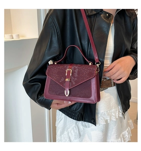 Detail of burgundy snakeskin crossbody bag with golden buckle on a black leather jacket