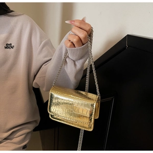 Macro view of metallic gold mini bag with crocodile texture and thin chain strap