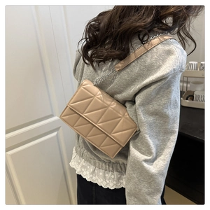 Close-up of beige quilted crossbody bag with chain strap on a woman shoulder