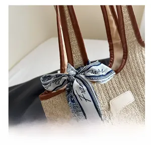 Detailed view of straw woven tote with brown leather trim and decorative blue silk scarf