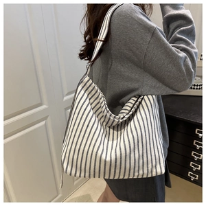 Side view of a large blue striped canvas tote bag worn over a casual grey sweater