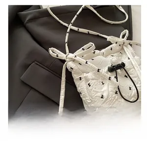 Detail of white bow-print drawstring bag showing pleated texture and fine shoulder strap