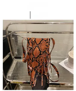 Detail of orange snake print crossbody bag featuring long fringe and leather strap