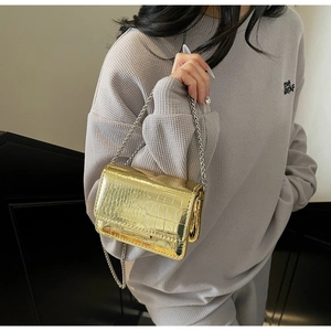 Close-up of golden croc-embossed mini bag with metallic chain strap worn by a model