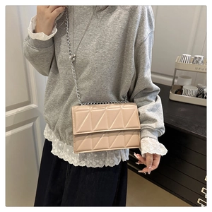 Detail of a beige quilted crossbody bag with silver chain strap worn by a model