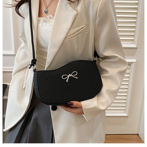 Close-up of black textured shoulder bag with silver metal bow charm on white suit