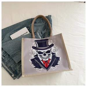 Détail du sac cabas en toile avec un crâne portant un haut-de-forme sur fond de tissu blanc