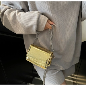 Detail of metallic gold mini crossbody bag with crocodile texture and silver chain strap