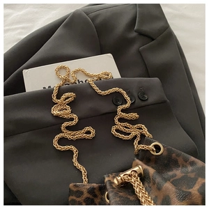 Close-up of leopard print bucket bag with golden chain strap on a blazer background
