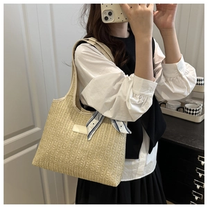 Detail of woven straw tote bag with blue geometric silk scarf on shoulder strap