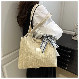 Detail of hand-woven straw tote bag featuring decorative silk scarf and leather patch