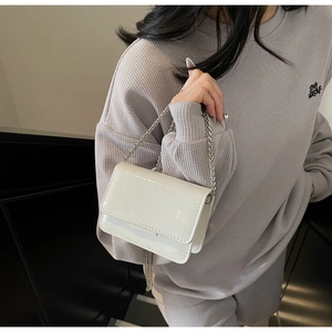 Detail of white patent leather mini bag with crocodile texture and silver chain strap