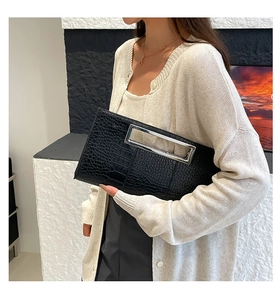Close-up of black crocodile embossed clutch bag with a large silver metal handle detail
