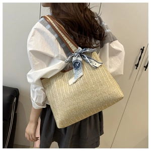Detail of a beige woven straw tote with brown leather strap and decorative silk scarf