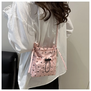 Pink quilted crossbody bag with black bow patterns and slim shoulder strap shown on model