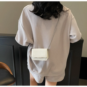 Back view of a mini white patent leather flap bag with silver chain on a casual outfit
