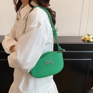 Green woven shoulder bag with silver bow accent and thick rope strap worn by model