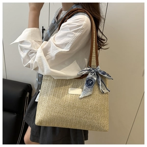 Detail of hand-woven beige straw tote bag with brown straps and floral silk scarf