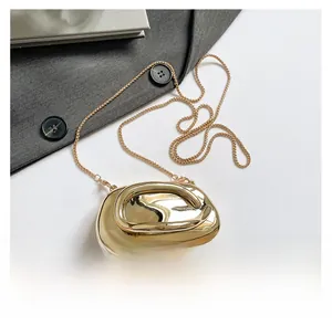 Detailed top view of gold pebble-shaped evening bag with metallic chain on white surface