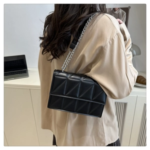 Close-up of black quilted shoulder bag with triangle stitching and silver metal chain