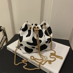 Close-up of cow print bucket bag with gold chain strap and pearl drawstring detail