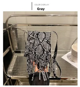 Detail of grey snakeskin crossbody bag with tassel and adjustable strap on a metal rack