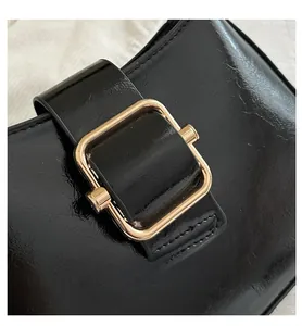 Close-up of black glossy oil wax leather bag with large golden square metal buckle detail