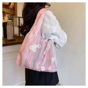 Gros plan du sac cabas rose avec broderie florale blanche et nœud en dentelle