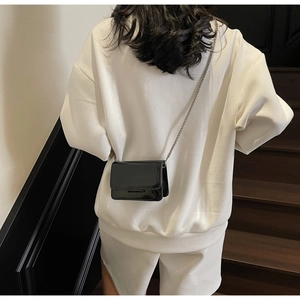 Close-up of a mini black patent leather crossbody bag with chain on a white sweatshirt