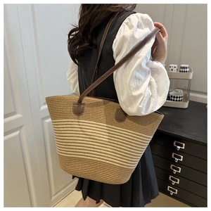 Detail view of woven straw tote bag with brown leather strap in natural indoor setting