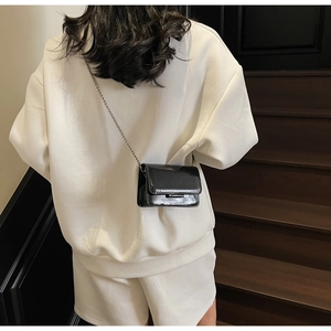 Close-up of black patent leather crossbody bag with silver chain on a model