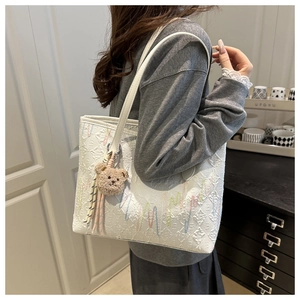 Detail of canvas tote bag with colorful embroidery and brown plush bear charm