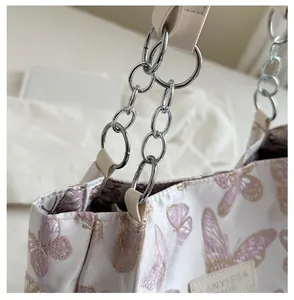 Detailed close-up of white butterfly tote bag with silver chain strap and leather tag