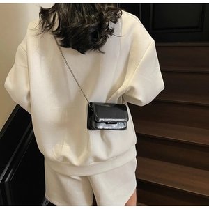 Back view of model wearing a black patent leather mini crossbody bag with silver chain