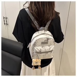 Detail of white backpack with butterfly pattern, calligraphy print and plush charm